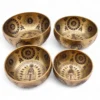 Set of 4 brass singing bowls etched with chakras and Om symbols for sound healing.