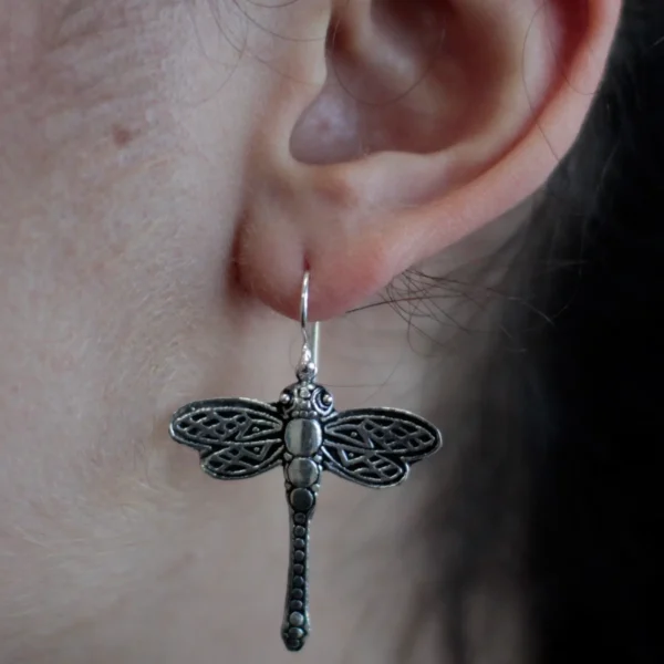 Close-up of a silver dragonfly filigree drop earring worn on an ear.