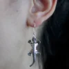 Quirky Jewellery Silver lizard drop earring with textured reptile design hanging from a person’s ear.
