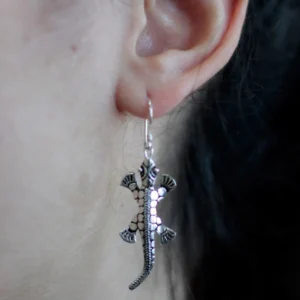 Quirky Jewellery Silver lizard drop earring with textured reptile design hanging from a person’s ear.