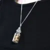 A silver chain necklace with a small glass bottle pendant containing gold fragments.