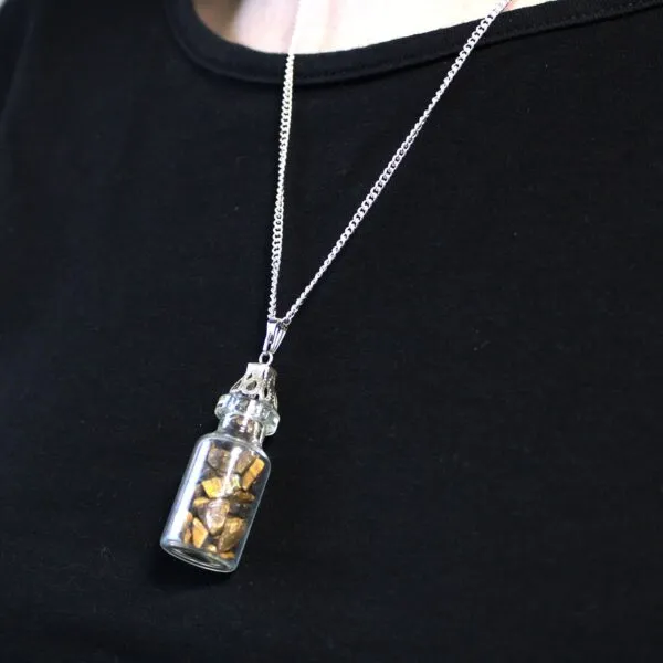 A silver chain necklace with a small glass bottle pendant containing gold fragments.