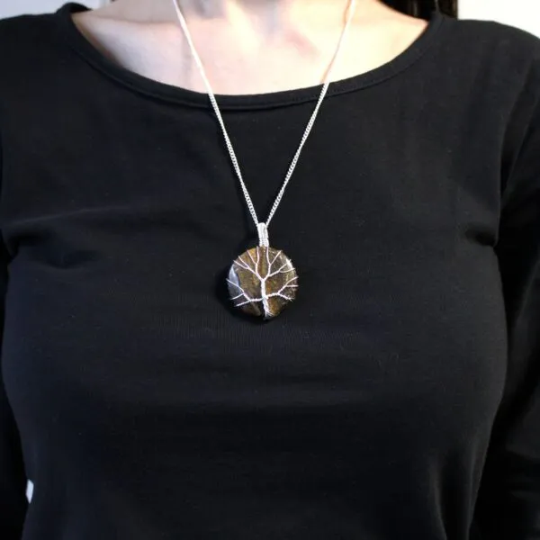 A silver tree of life pendant on a brown stone necklace worn over a black top.