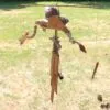 A handmade wooden dragon wind chime hanging outdoors above sunlit grass and pinecones.
