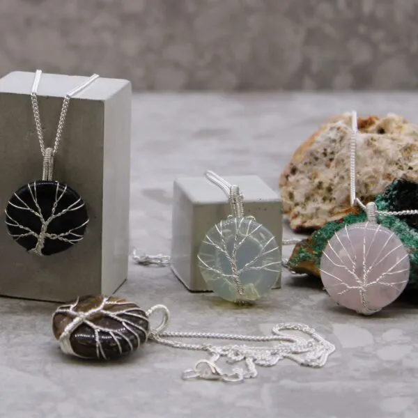 Silver Tree Of Life Gemstone Pendants - Mixed Stone Colours Four silver Tree of Life gemstone pendant necklaces displayed on grey stone blocks and rocks.