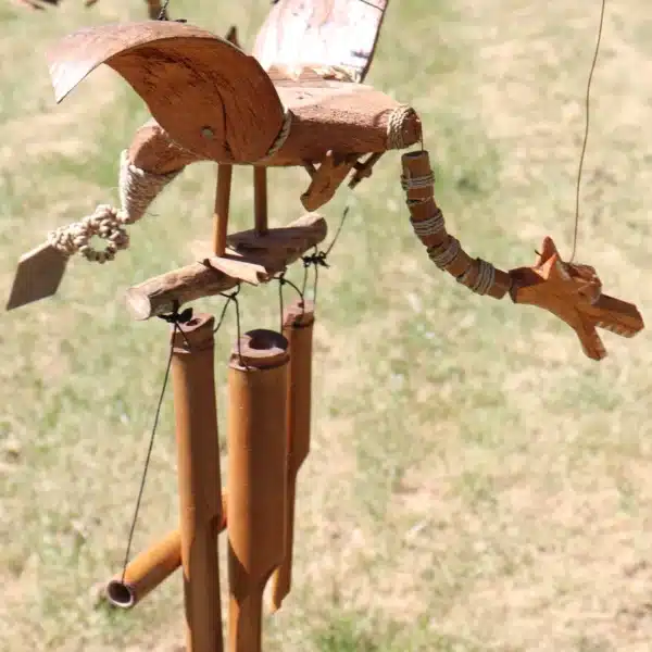 Handcrafted wooden bird-shaped wind chime with bamboo tubes hanging outdoors in natural sunlight.