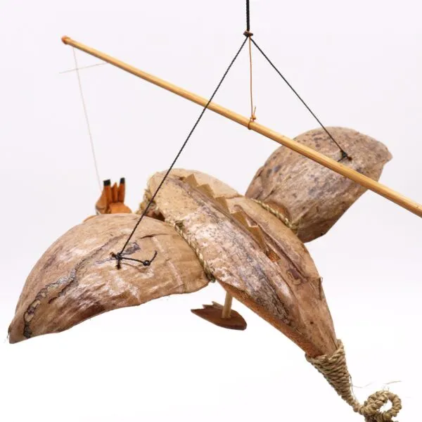Handcrafted bird sculpture made from dried palm leaves and wood, suspended with strings against white background.