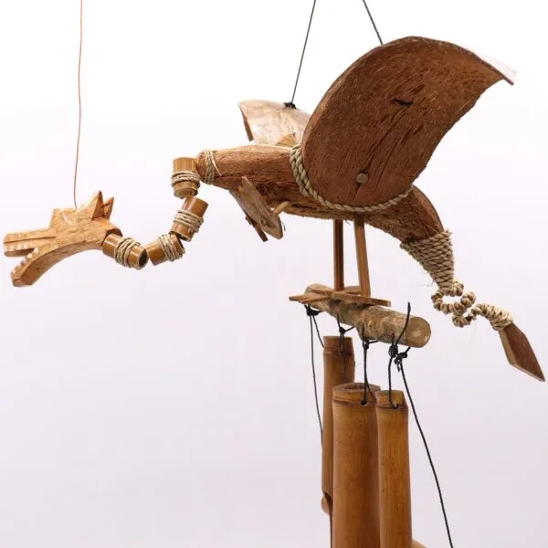 Handcrafted wooden dragon wind chime with bamboo tubes and natural rope details hanging outdoors.