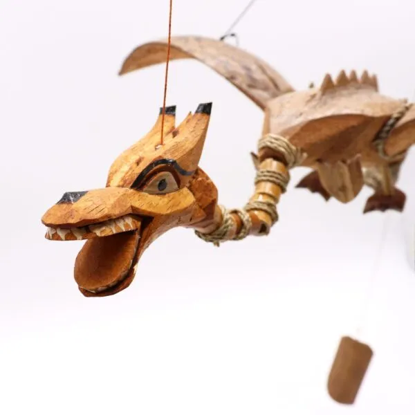 A hand-carved wooden dragon marionette with detailed features and strings against a white background.