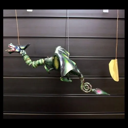 A colourful dragon marionette with green wings and blue head suspended by strings against a dark background.