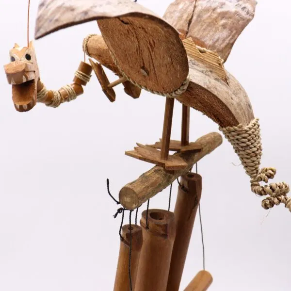 Hand-carved wooden dragon sculpture perched above bamboo wind chimes made from natural materials.