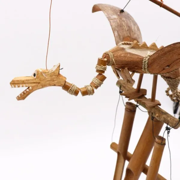 A handcrafted wooden dragon marionette with bamboo wings suspended by strings against a white background.