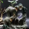 Elephant Tabletop Fountain Resin Grey - Crystal Ball Waterfall Two sculpted elephants with a crystal ball tabletop fountain surrounded by greenery and gentle flowing water.