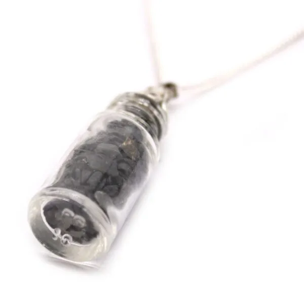 A small glass vial pendant necklace filled with dark natural stones on a silver chain.