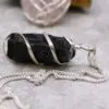 A black raw stone pendant wrapped in silver wire on a light grey surface.