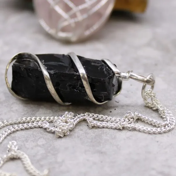 A black raw stone pendant wrapped in silver wire on a light grey surface.