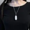 A person wearing a silver necklace with a wire-wrapped raw rose quartz crystal pendant.