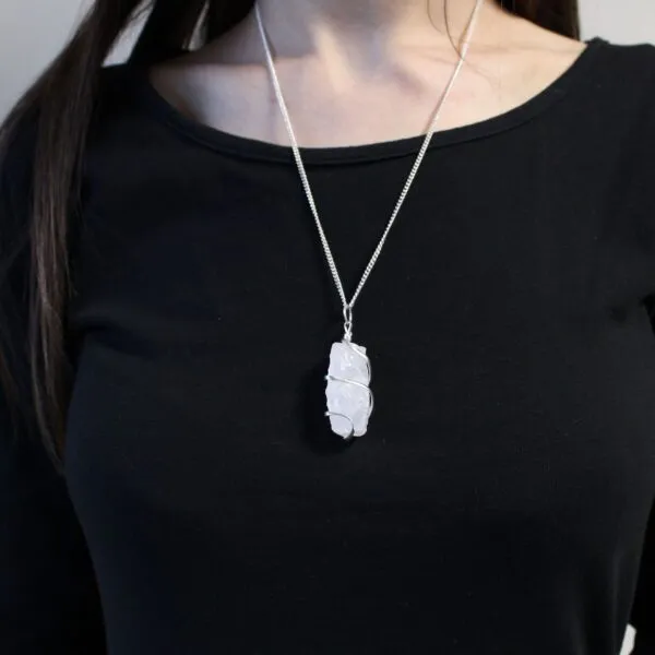 A person wearing a silver necklace with a wire-wrapped raw rose quartz crystal pendant.