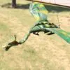 A green and yellow dragon marionette hanging by strings outdoors on sunlit grass.