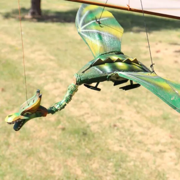 A green and yellow dragon marionette hanging by strings outdoors on sunlit grass.