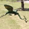 A colourful wooden dragon marionette hanging outdoors against a bright grassy park background.