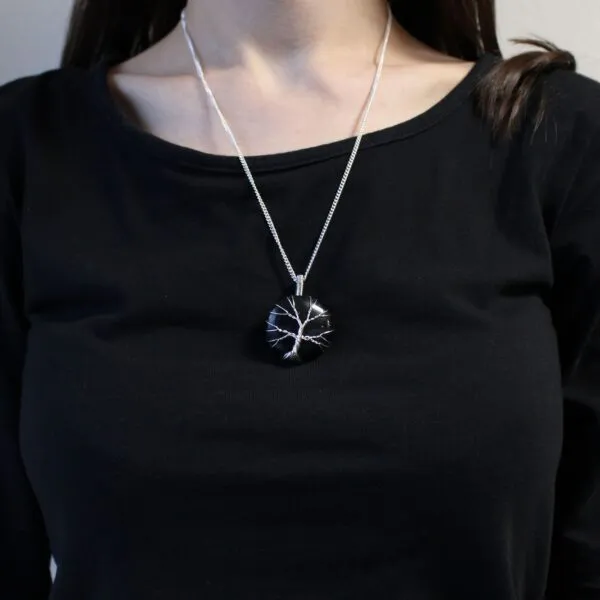 A silver tree of life pendant on a fine chain worn over a black long-sleeved shirt.