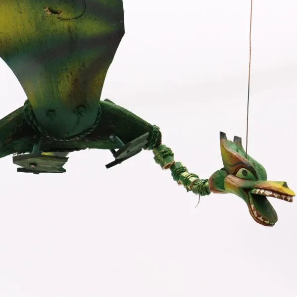 A handcrafted green wooden dragon marionette with painted details hanging against a plain white background.