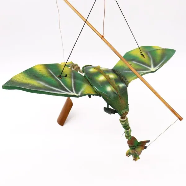 A handcrafted wooden dragon marionette with green and yellow wings suspended by control strings.