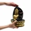 A small golden Buddha tabletop water fountain with cascading bowls and a lotus base held in hands.