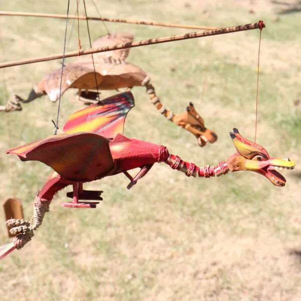 Handcrafted red wooden dragon marionette hanging outdoors with painted wings and rustic string details.