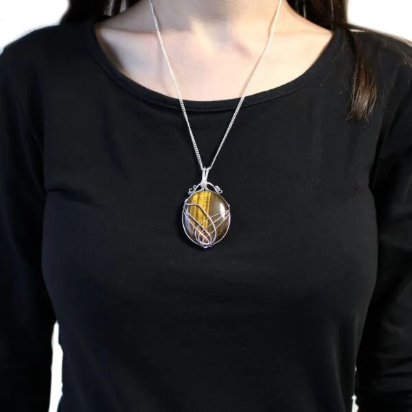 A silver wire-wrapped tiger’s eye pendant on a delicate chain worn over a black shirt.