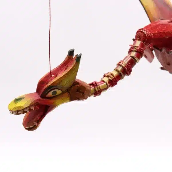 A colourful wooden dragon sculpture hanging by a red string against a plain white background.