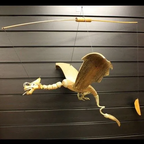 A handcrafted wooden dragon mobile suspended mid-air against dark panelled background.