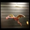 A red and gold dragon marionette puppet hanging against a dark slatted background.