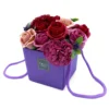 Purple gift box with artificial red and pink rose bouquet and green leaves arrangement.