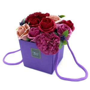 Purple gift box with artificial red and pink rose bouquet and green leaves arrangement.