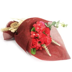 Handcrafted red soap flower bouquet with roses, green foliage, and rustic raffia in red mesh wrap.