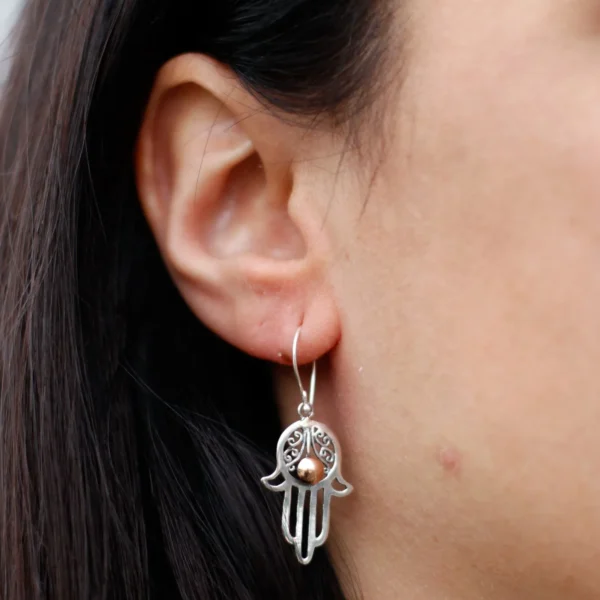 Close-up of a woman wearing a sterling silver Hamsa hand earring with copper accent.