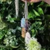 Hand holding silver wire-wrapped crystal pendant necklaces gleaming against a lush green garden background.