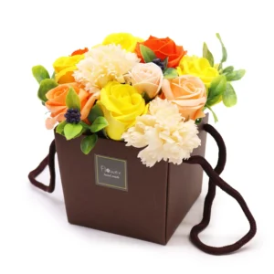 A colourful artificial flower bouquet arranged in a brown handmade gift box with fabric handles.