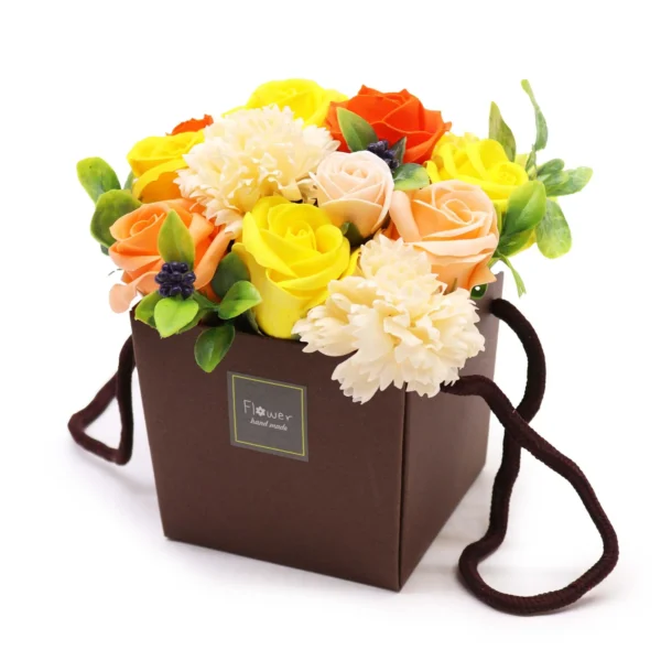 A colourful artificial flower bouquet arranged in a brown handmade gift box with fabric handles.