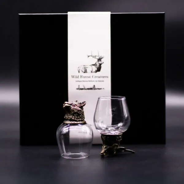 Wild Forest Creatures Bronze Glass Set - Animal Head Design Two clear glasses with bronze animal heads set before a black box labelled “Wild Forest Creatures”.