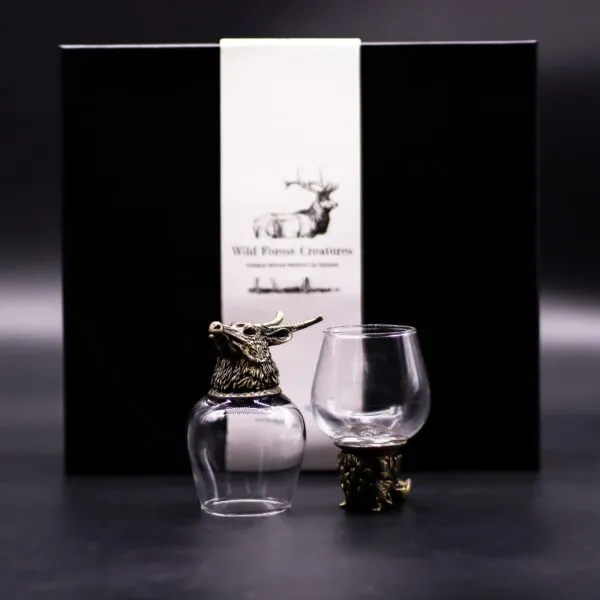 Vintage Bronze Whiskey Glasses Black Gift Box - Stag Design Two bronze-bottom whiskey glasses with stag designs displayed before a black “Wild Forest Creatures” gift box.