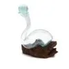 A clear hand-blown glass vessel with a bluish tint resting on natural driftwood.