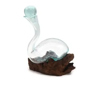 A clear hand-blown glass vessel with a bluish tint resting on natural driftwood.
