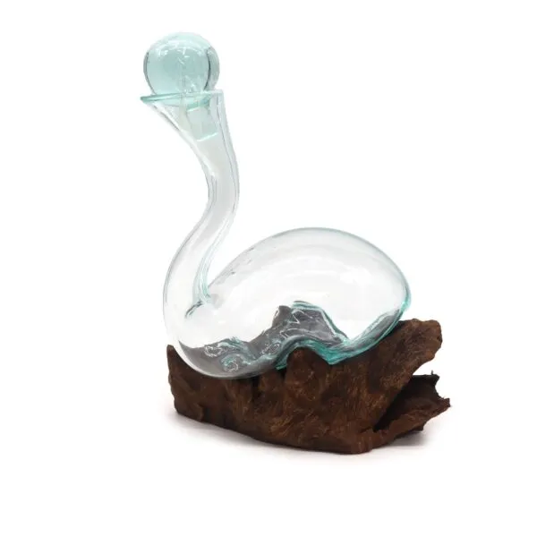 A clear hand-blown glass vessel with a bluish tint resting on natural driftwood.