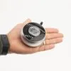 A person holding a small circular silver and black portable speaker in their open hand.