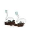 Two swan-shaped hand-blown glass sculptures with blue-green tint resting on rustic wooden bases.