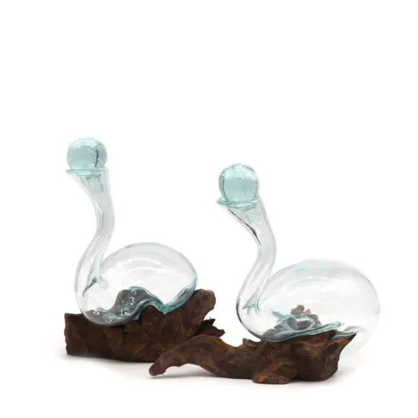 Two swan-shaped hand-blown glass sculptures with blue-green tint resting on rustic wooden bases.