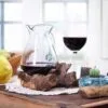 A rustic wine table with red wine decanter, glass, green grapes, pear, and cactus candle.